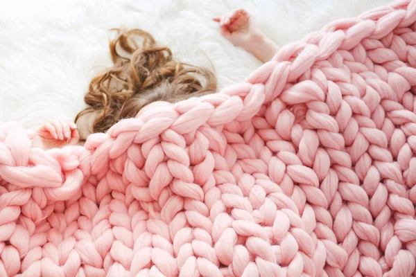 Young woman with long brown hair sleeping under warm knitted peach color throw blanket