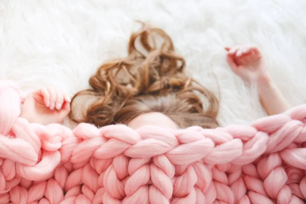 Young woman with long brown hair sleeping under warm knitted peach color throw blanket