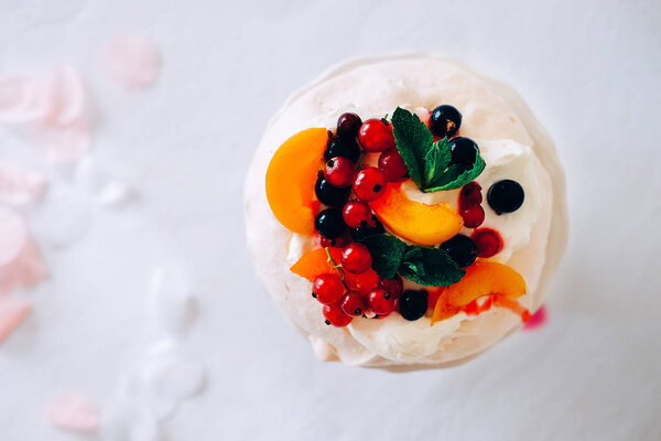 Tasty Pavlova dessert on porcelain plate with white meringue, cream and fruit. Traditional Australian sweet food.