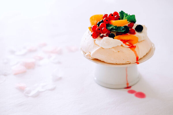 Tasty Pavlova dessert on porcelain plate with white meringue, cream and fruit. Traditional Australian sweet food.
