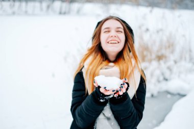 Çekici sarışın genç yetişkin kadın siyah parka, kot pantolon, pembe deri çizme ve sırt çantası ve bej şal gündelik kıyafeti giymiş ilk kar ile eğleniyor