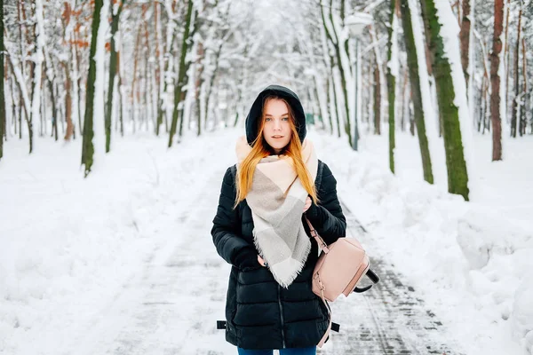 迷人的金发碧眼的年轻成年妇女走在冬季森林充满了雪穿着休闲服装的黑色帕卡 牛仔裤 粉红色皮靴和背包和米色披肩 — 图库照片