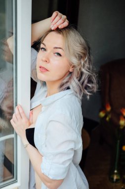 Dairesinde bir kadın pencere kenarına yakın giyiniyor. Fransız tarzı. Modern renkli saç stili.