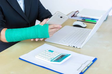 iş kadını akıllı telefon tutarak ve ofis, kırık el odak içinde laptop üzerinde kolundaki yeşil döküm ile.