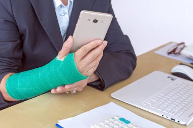 iş kadını akıllı telefon tutarak ve ofis, kırık el odak içinde laptop üzerinde kolundaki yeşil döküm ile.