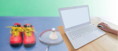 Badminton spor arka plan, modern dizüstü bilgisayar ve el ahşap masa üzerinde bulanık badminton raket ve kırmızı ayakkabı sahası üzerinde raketle izole fare kullanma