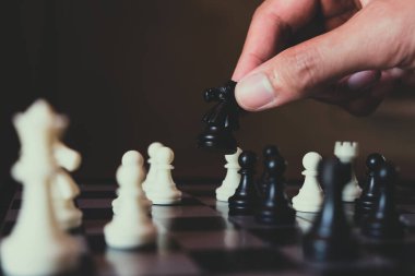 Hand of businessman making move with black knight on chess board