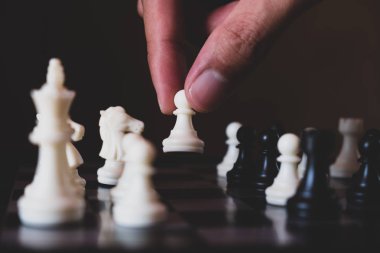 Hand of businessman making move with white pawn on chess board