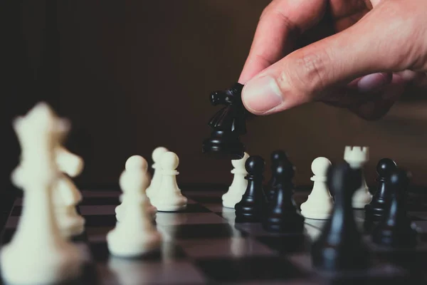 Hand of businessman making move with black knight on chess board