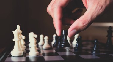 Hand of businessman making move with black rook on chess board