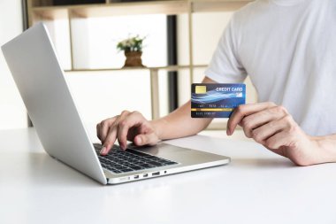 Bir adamın eli kredi kartını tutuyor ve internetten alışveriş için bilgisayar defteri kullanıyor..  