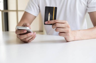 Bir adamın eli kredi kartını tutuyor ve internetten alışveriş yapmak için cep telefonunu kullanıyor..