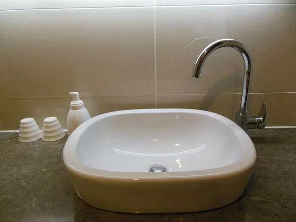 Mermer bir banyo, klasik musluk, sabunluk ve iki bardak içinde üzerinde beyaz seramik lavabo 