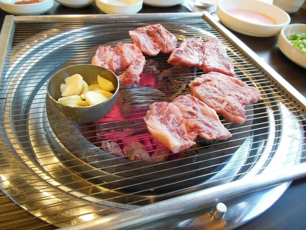 Korean style barbecue on table with closeup of red meat being grilled on charcoal