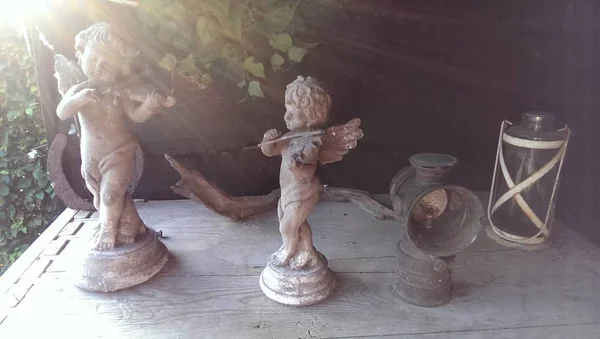 Cherubs (melek) üzerlerine göksel güneş ışınları gibi parlayan güneş ışığı ile heykel ve fener bahçe ahşap raf taş; Zen gibi sahne için meditasyon