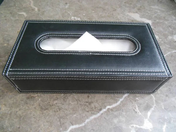 Black leather box with white soft paper tissues on marble surface, ready for hygiene purposes