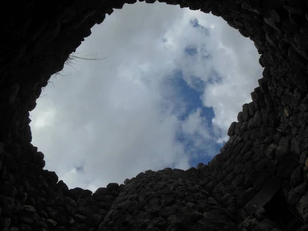 UNESCO mirası bölgesinde Sardunya 'daki tarihi Nuraghe kulesinin yuvarlak deliği ile bulutlu gökyüzüne bakıyor