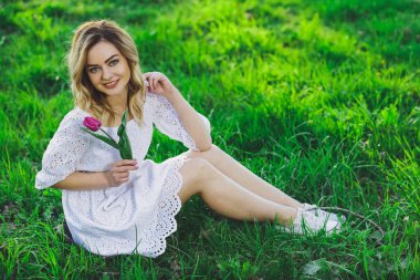 Arka plan yeşil çim üzerinde bir çiçek lale ile beyaz elbiseli Genç güzel sarışın kız