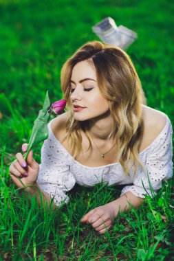 Arka plan yeşil çim üzerinde bir çiçek lale ile beyaz elbiseli Genç güzel sarışın kız