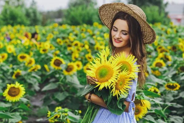 Young beautiful girl in dress and hat in field with sunflowers