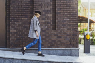 Genç kız güzel bir ceket, kot pantolon ve bir tuğla duvar arka plan üzerine şapka