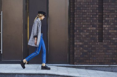 Genç kız güzel bir ceket, kot pantolon ve bir tuğla duvar arka plan üzerine şapka