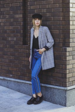 Genç kız güzel bir ceket, kot pantolon ve bir tuğla duvar arka plan üzerine şapka