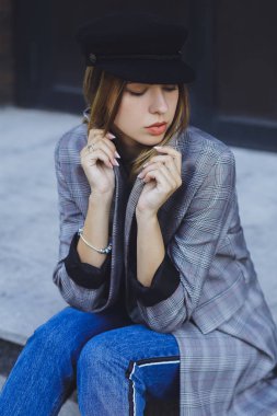 Genç kız güzel bir ceket, kot pantolon ve bir tuğla duvar arka plan üzerine şapka