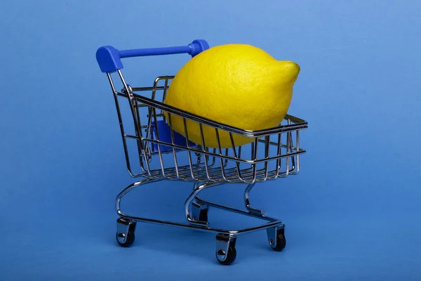 ショッピングカート 青の背景にショッピングトロリーでレモン — ストック写真