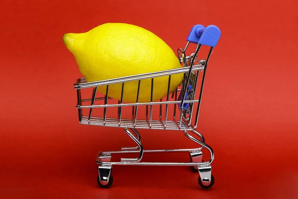 ショッピングカート 赤の背景にショッピングトロリーでレモン — ストック写真