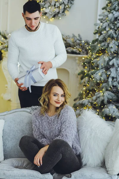 The guy gives a gift to the girl on the background of the Christmas tree. Christmas background