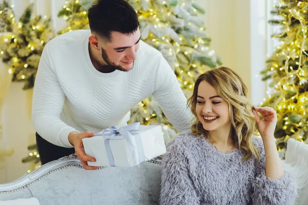 The guy gives a gift to the girl on the background of the Christmas tree. Christmas background
