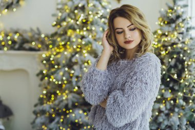 Yeni yıl hediyeleri ile Noel ağacı yakınındaki ellerinde bir hediye ile gri süveterli genç güzel sarışın kadın
