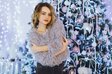 Yeni yıl hediyeleri ile Noel ağacı yakınındaki ellerinde bir hediye ile gri süveterli genç güzel sarışın kadın