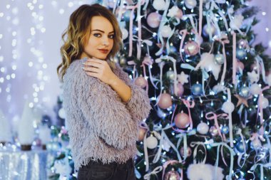 Yeni yıl hediyeleri ile Noel ağacı yakınındaki ellerinde bir hediye ile gri süveterli genç güzel sarışın kadın