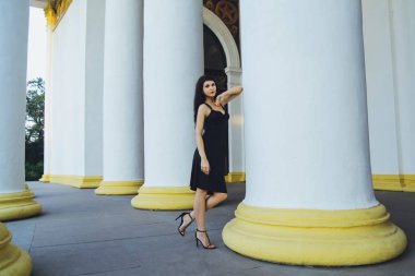 Beyaz sütunları yakınındaki siyah elbiseli Genç güzel esmer kız