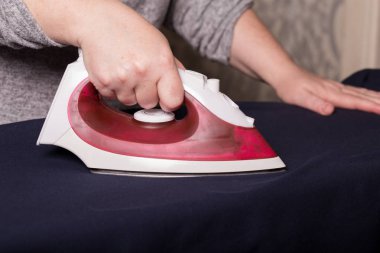 Kıyafetleri ütülüyorum. Kadın elleri kırmızı bir demir kaplama ile giysileri ütülüyor.. 