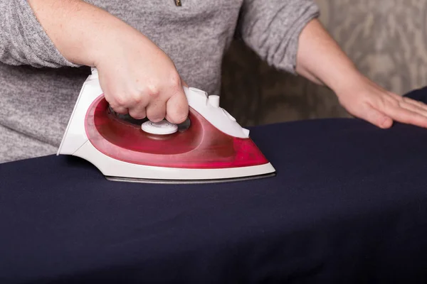 Ironing clothes. Female hands are ironing clothes with a red iron close-up.