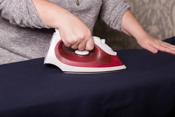 Ironing clothes. Female hands are ironing clothes with a red iron close-up.