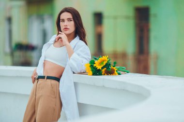 Şehirde, şapkalı, siyah saçlı güzel bir kadın bir buket ayçiçeği için el ele tutuşuyor ve başka tarafa bakıyor. Şık ve şık bir kız.