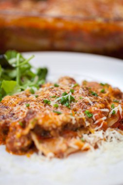 Lazanya bolognese peynirli yeşil salata ile beyaz tabakta görünümü Kapat