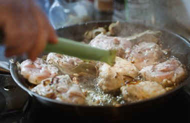 Erkek el mutfak maşa ile soğan tavada ızgara ve kızarmış tavuk bacak biftek üzerinde beyaz şarap soslu otlar karıştırma tutarak