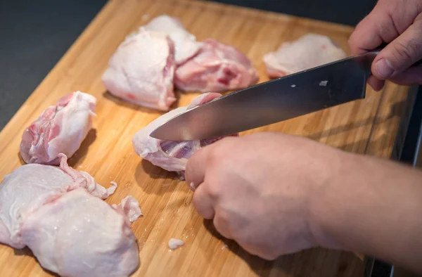 Man cutting chicken leg steaks on cutting board