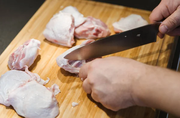 Man cutting chicken leg steaks on cutting board