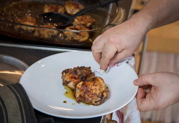 man serving baked chicken leg steaks on white wine sauce and onions minimalistic on white plate