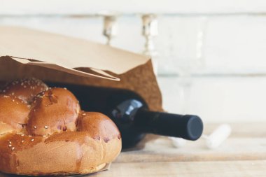 Shabbat or Sabbath grocery shopping composition with a traditional sweet fresh loaf of challah bread with a bottle of red kosher wine on a vintage wood background clipart