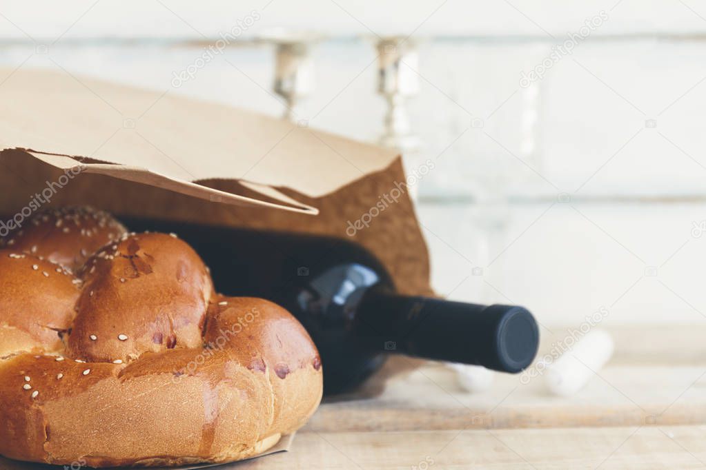 Shabbat or Sabbath grocery shopping composition with a traditional sweet fresh loaf of challah bread with a bottle of red kosher wine on a vintage wood background