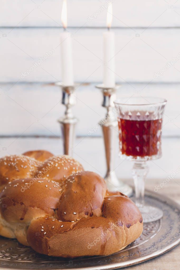 Shabbat or Sabbath kiddush ceremony composition with a traditional sweet fresh loaf of challah bread, glass of red kosher wine and candles on a vintage wood background 