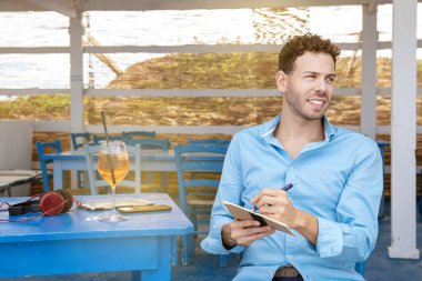 Solak genç adam plaj barında oturmuş ödevlerini yapıyor.