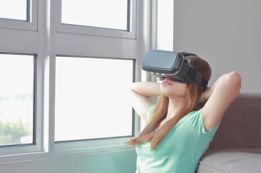 Evde sanal gerçeklik gözlüklü genç kadın. Bir sanal gerçeklik kulaklık takan için sanal gerçeklik sağlar başa takılan bir aygıt olduğunu.